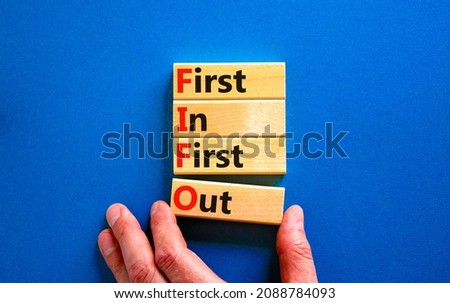 FIFO first in and out symbol. Concept words FIFO first in first out on wooden blocks. Beautiful blue table, blue background. Businessman hand. Business FIFO first in and out concept. Copy space.