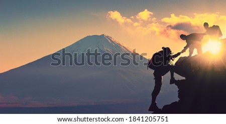Young asian couple hikers climbing up on the peak of mountain near mountain fuji. People helping each other hike up a mountain at sunrise. Giving a helping hand. Climbing. Helps and team work 