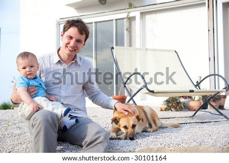 father with his baby son and dog in front of a house