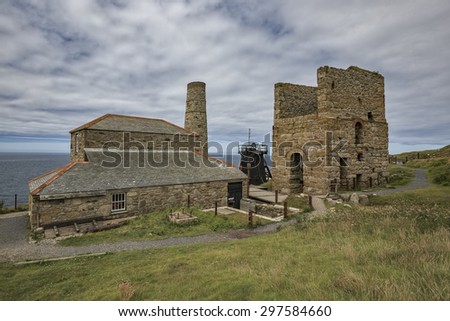A Cornish tin mine sits at the top of a hill against the backdrop of the ocean under a cloudy sky