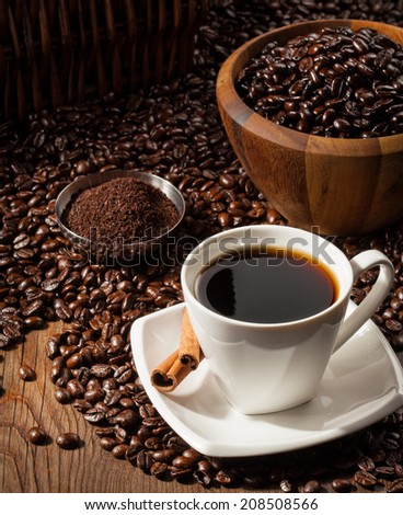 Black Coffee in a white Coffee cup with whole and freshly ground beans on a wooden table. Dark background.
