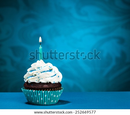 Chocolate Cupcake with  icing and lit birthday candle over a blue background