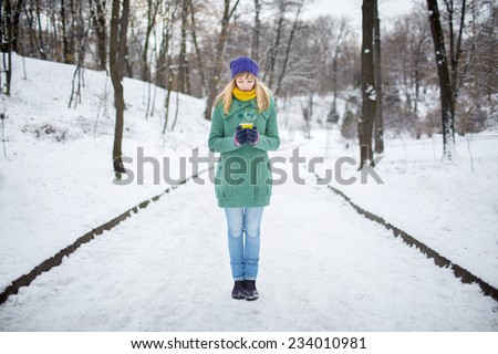 Girl in green coat holding a cup of coffee latte with milk. Lonely woman stands on a snowy winter deserted street in the park.