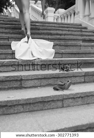 Black and white photography. Slender women\'s legs. Woman takes off dress on the stairs