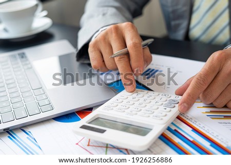Asian male finance staff is calculating by using a calculator. Investment results to report to his boss at the meeting. On the table in the office, the concept of calculating investment results