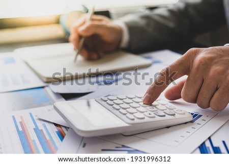 Asian male finance staff is calculating the investment results to deliver a report to his supervisor at the meeting. On the table in the office, the concept of calculating investment results 