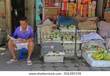 HANOI, VIETNAM - JUNE 1, 2015: man is sitting on a chair with newspaper nearly stand with vegetables and fruits