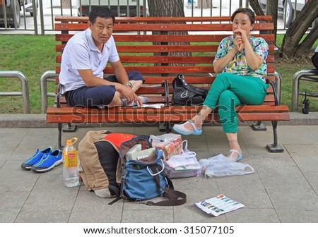 BEIJING, CHINA - JULY 4, 2015: man and woman are waiting something on the bench in park of Beijing