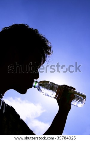 Silhouette of a man drinking from a plastic bottle shot against a blue sky