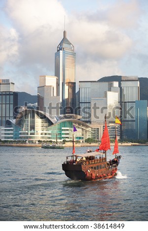 Sunset view of a traditional, junk ship with wind sails shot against modern cityscape of Hong Kong island