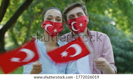 Two young people are waving the Turkish flag while looking at the camera. They wear a medical mask in the form of a Turkish flag to protect them from the virus. Stock fotó © 
