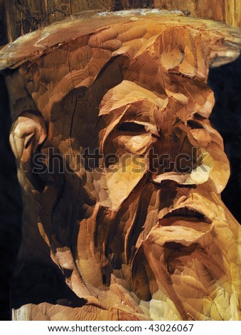 Man\'s face carved in wood under harsh lighting