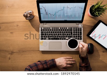 Man controlling cryptocurrency traffic with laptop from home. The man who earns bitcoin is comfortably drinking coffee.