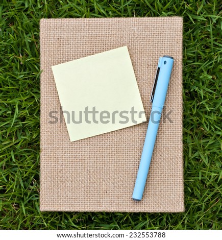 Notepaper and pen on the note book, Green grass background,yellow stick note