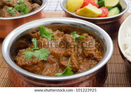 A bowl of Madras butter beef curry with rice, salad and another curry bowl in the background