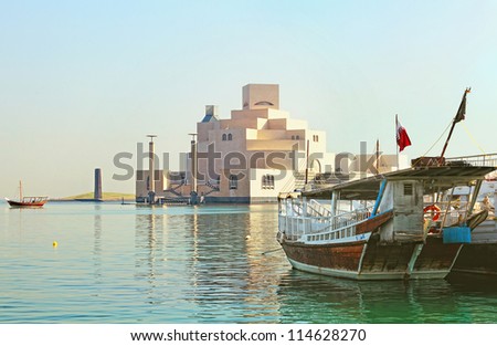 Qatar\'s museum of Islamic Art on its man-made island beside Doha Corniche, with dhows moored in the bay surrounding it.
