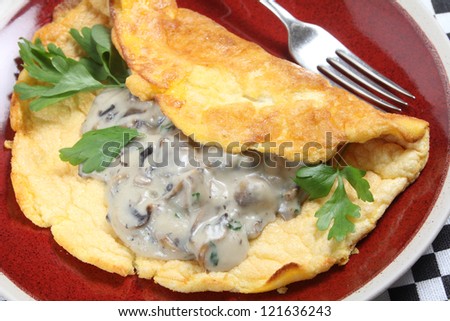 A homemade souffle omelet served with mushrooms in a creamy sauce, garnished with flat-leaf parsley, high angle view