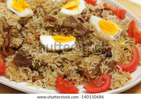 Closeup view of a serving dish of homemade beef biryani garnished with boiled eggs and tomato