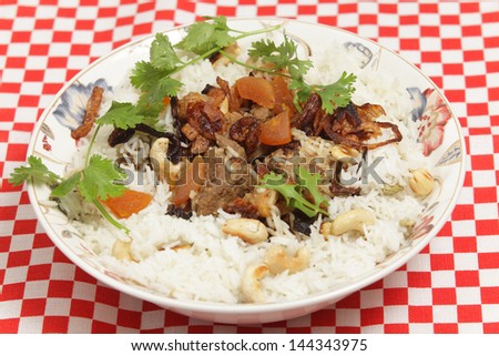 A serving bowl of home-made biryani-type lamb curry, cooked with dried apricots and yoghurt and garnished with toasted cashews, fried onions and coriander, served with cardamom-flavoured basmati rice.