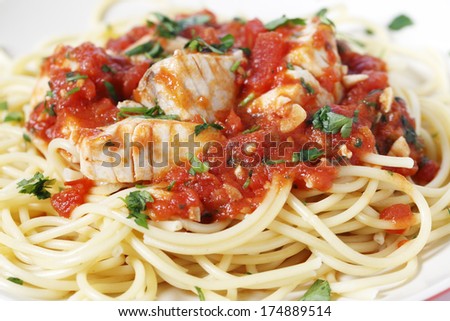 Spaghetti all\'arrabbiata with fish, garnished with parsley, seen closeup form the side. The sauce is made from tomato, garlic, olive oil and flaked chillis.