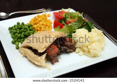 A steak, kidney, mushroom and carrot pudding, in a suet pastry crust, served with lettuce, potatoes, peas and sweetcorn. Steak and kidney pudding is a traditional English dish