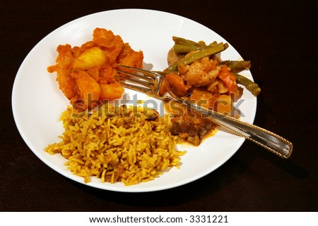 An Indian vegetarian meal: coconut pilau rice with vegetable curry and Punjabi potato curry on a dark wood table.