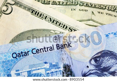 A high-value Qatari 500 riyal banknote, on top of US currency notes. Concern over the impact of the falling dollar may lead Qatar (and other oil states) to move or end the dollar peg.
