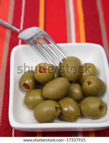Green stuffed olives on a dish with a fork, on a cloth