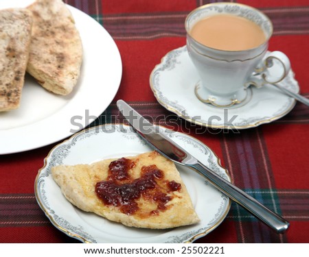 An Irish-style tea break with soda farl (flat soda bread triangles) strawberry jam and a cup of tea on a tartan table cloth.