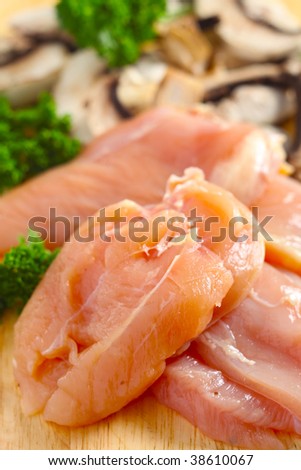 The ingredients for a chicken and mushroom dish, chicken breasts, sliced mushrooms, parsley and onion, on a chopping board