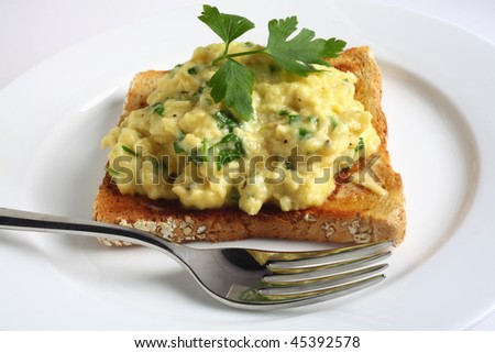Scrambled egg with chopped fresh parsley and brown toast on a plate with a fork. Parsley gives a delicious flavour to the dish and is a traditional addition.