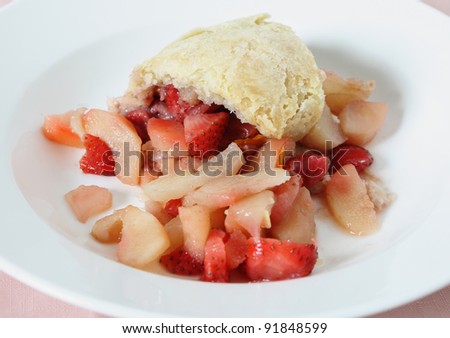 A portion of steamed pear and strawberry pudding in a suet pastry crust served in a white bowl