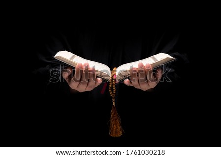 The image of a Muslim woman's hand, Islamic prayer, and her hand holding a quran and rosary beads or tasbih. Arabic word translation : The Holy Al Quran (holy book of Muslim)