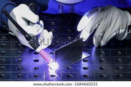 TIG welder with welding gloves is holding welding torch of a welding machine and welding stainless steel while on a job training in an aerospace factory workshop. Photo stock © 
