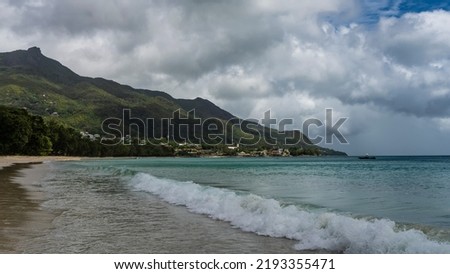 Turquoise ocean waves roll onto the sandy beach and foam.  A green hill against the sky and cumulus clouds. Seychelles. Mahe. Beau Vallon Photo stock © 