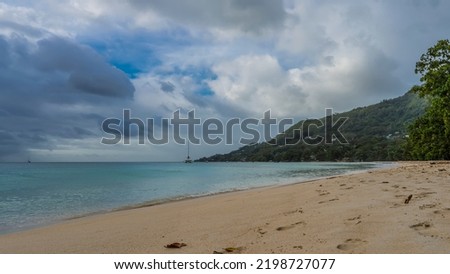 A beach on a tropical island. Footprints in the sand. The turquoise ocean is calm. A green hill against a background of blue sky and clouds. Seychelles. Mahe. Beau Vallon Photo stock © 