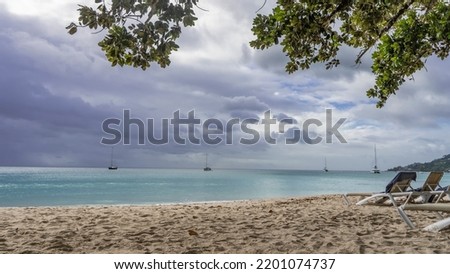 The sun beds are on the sandy beach. The turquoise ocean is calm. Yachts in the distance. Clouds in the blue sky. In the foreground are green tree branches. Seychelles. Mahe. Beau Vallon Photo stock © 