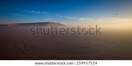 Four hot air balloons flying in the mist over a dry land with mountains on the background