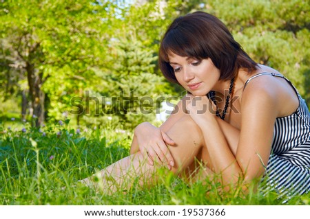 Young beautiful woman sits on a grass and thinks