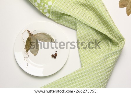 Still Life with laurel leaves and bell pepper on a white plate on a background of green towel