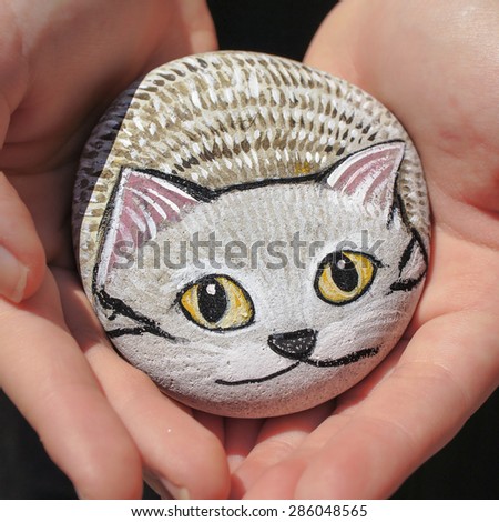 KYOTO, JAPAN : MAY 30, 2015 : Photo of handmade stone painted as a tabby grey cat, was holding by female hands. Selective Focus, Blur Background.