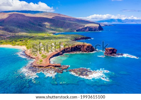 Aerial view of Lanai, Hawaii featuring Hulopo'e Bay and beach, Sweetheart Rock (Pu'u Pehe), Shark's Bay, and the mountains of Maui in the background.