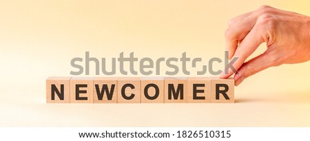 The hand puts a wooden cube with the letter R from the word NEWCOMER. The word is written on wooden cubes standing on the yellow surface of the table. Photo stock © 