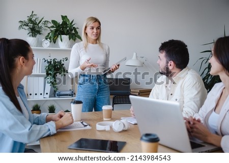 Business team of male and female colleagues sitting in the office and listening to speech of their partner. Blonde woman standing with the tablet and speaking  Stock fotó © 