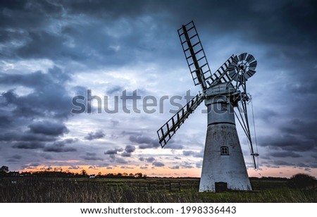 A mill in a field against the background of sunset. Sunset mill view. Windmill at sunset. Sunset windmill scene