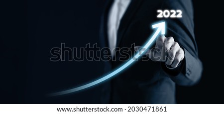 Smart businessman pointing graph future growth plan in 2022 on dark blue background. Business development and growth concept. Artificial intelligence (AI) support to increase business performance.