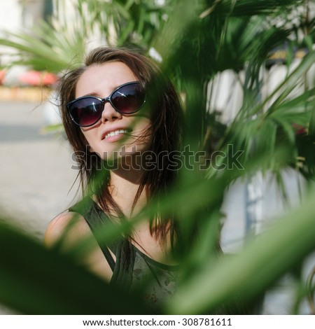 Its great to start a new day discovering city. Beautiful girl in sunglasses standing between palm leaves at old town.