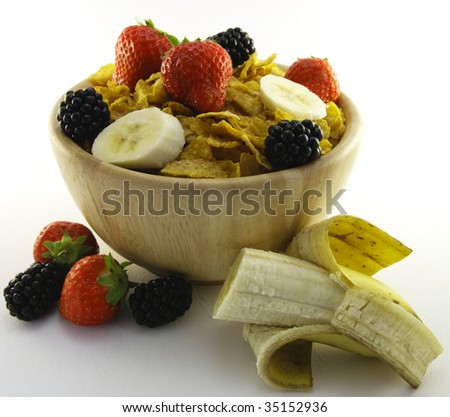 Cornflakes with strawberries, blackberries and banana in a round wooden bowl on a white background