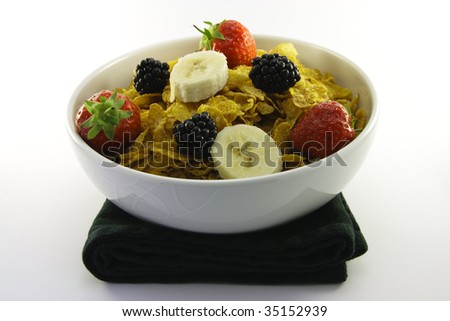 Cornflakes with strawberries, blackberries and banana in a round white bowl with a black napkin on a white background