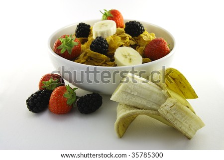 Cornflakes with strawberries, blackberries and banana in a round black bowl on a white background
